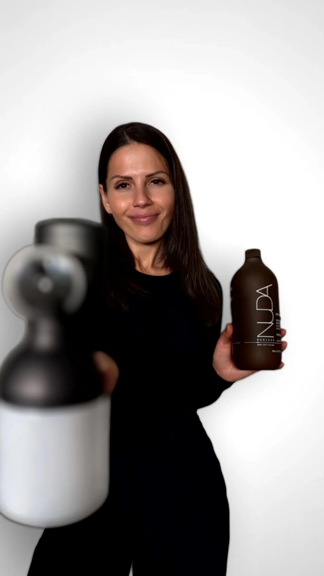 Ana Maria, artiste spray tan certifiée NUDA de GLOW17, avec son pistolet et une bouteille NUDA